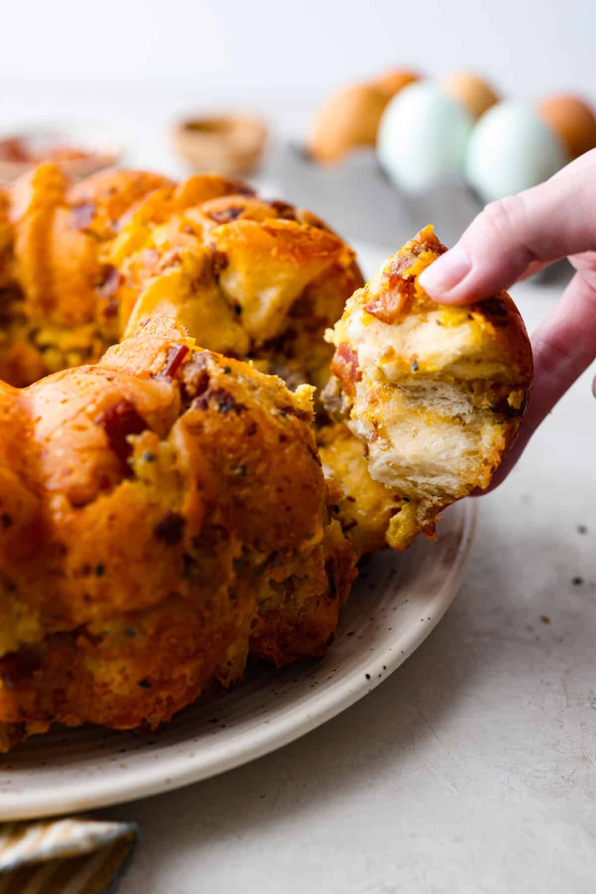 Side shot of someone pulling a piece of the savory breakfast monkey bread from the whole. 