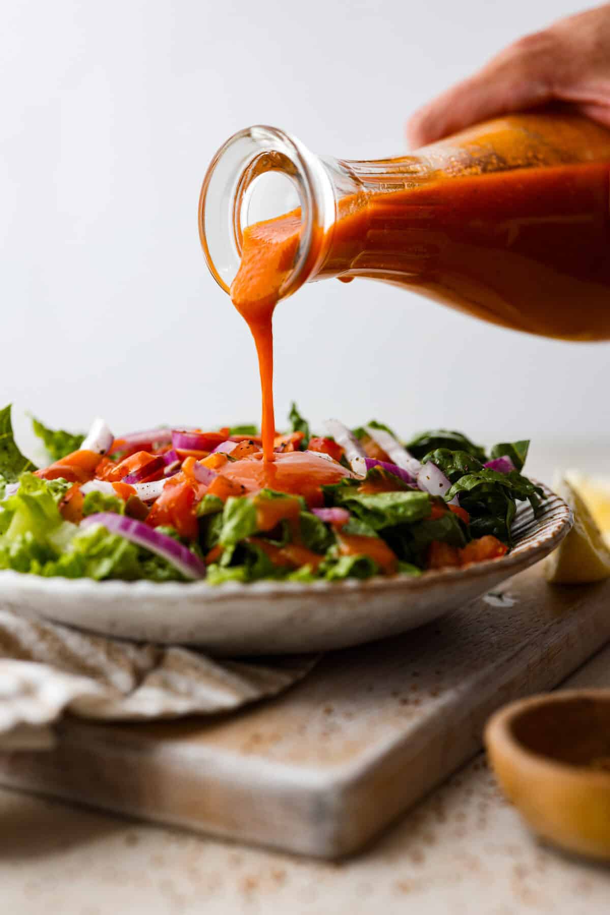 Side shot of someone pouring dressing over a plated salad. 