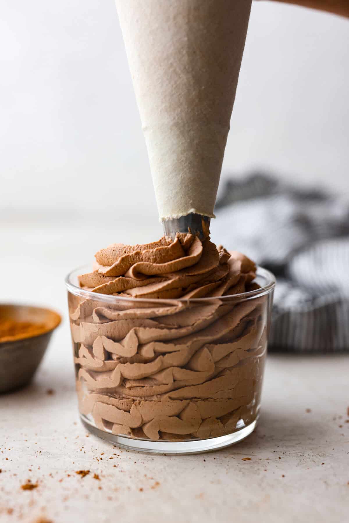 Side shot of someone piping chocolate whipped cream into a small glass container. 