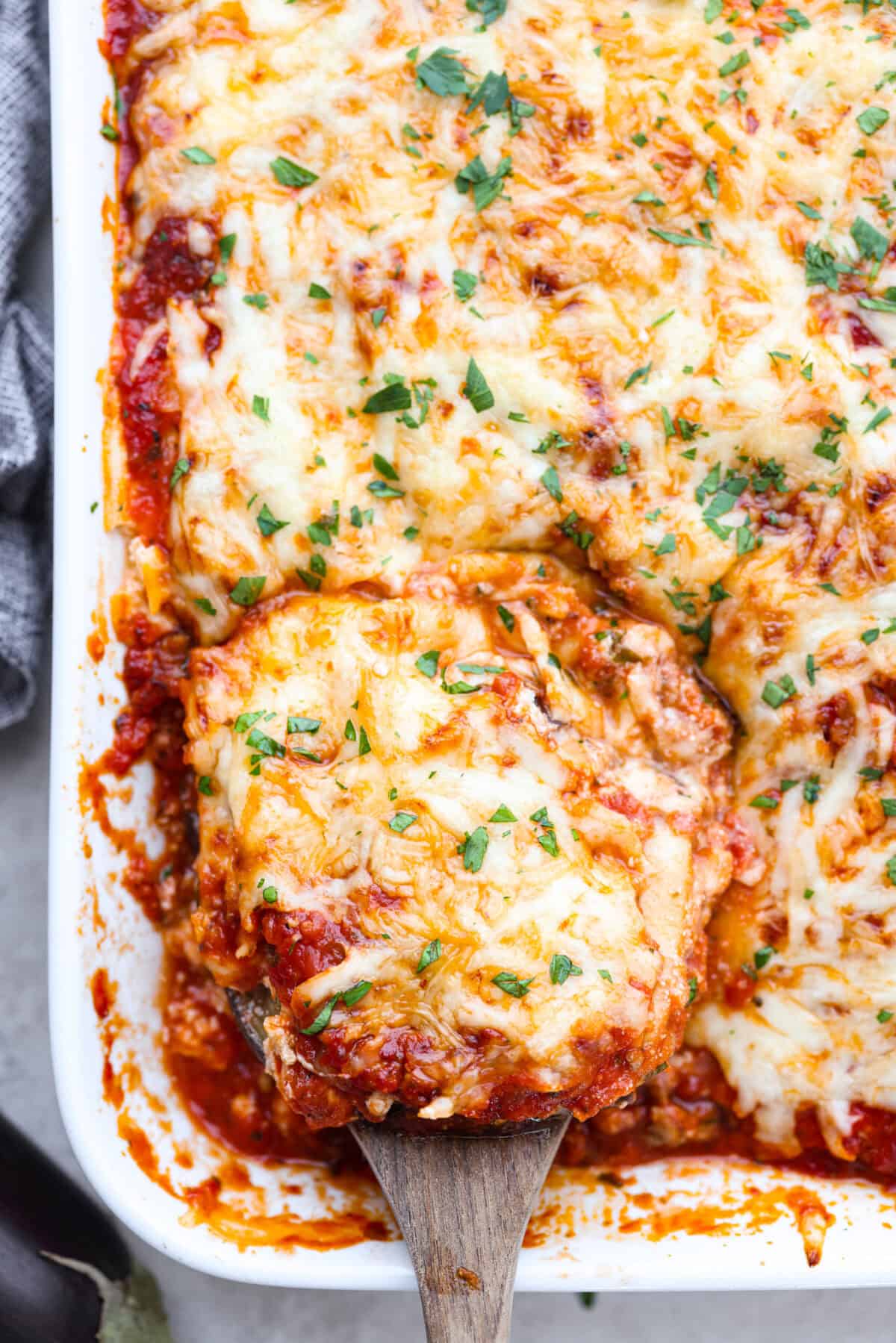 Close top view of the eggplant lasagna in a casserole dish with a wood serving spatula.