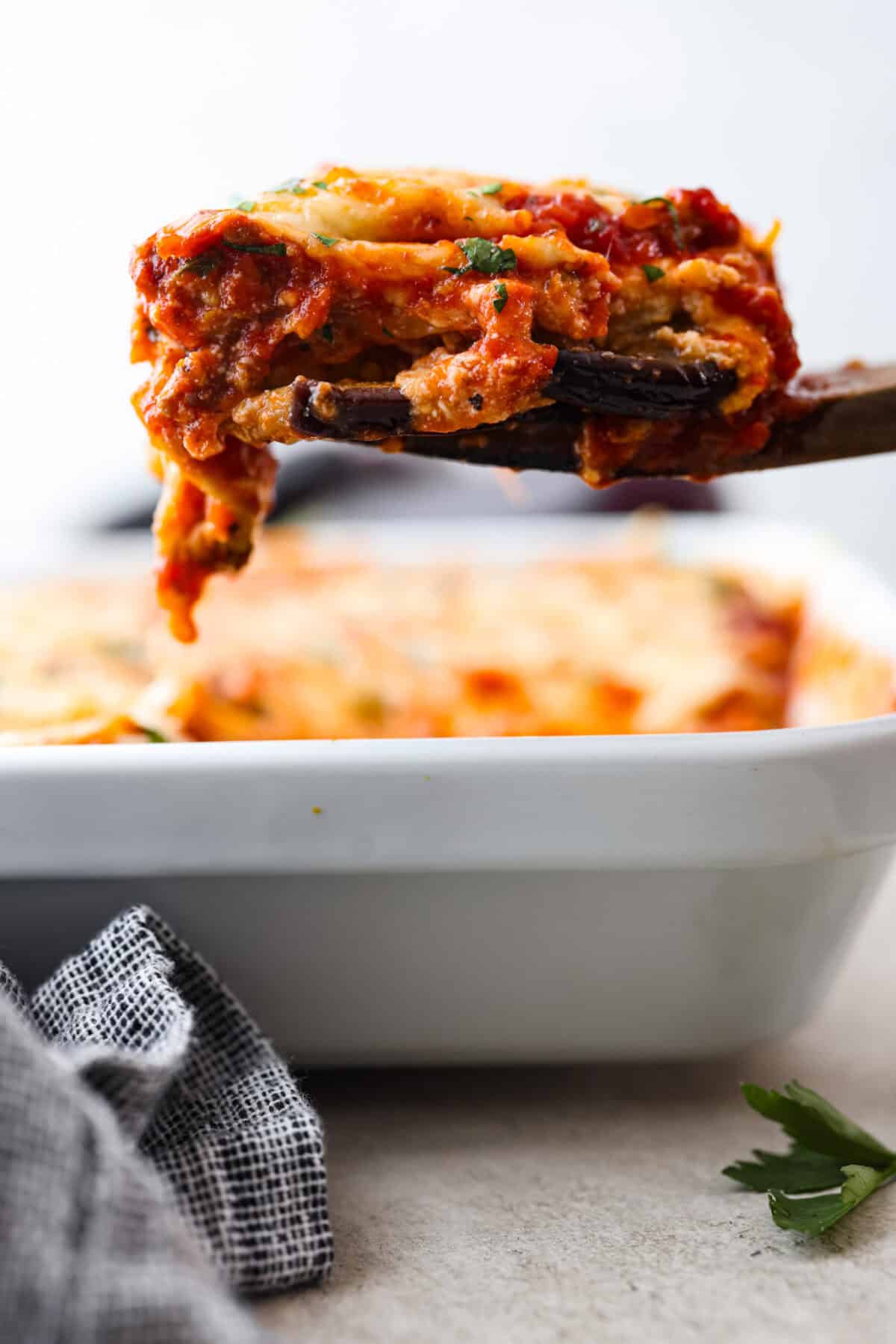 Close side view of a slice of eggplant lasagna lifting from the dish.