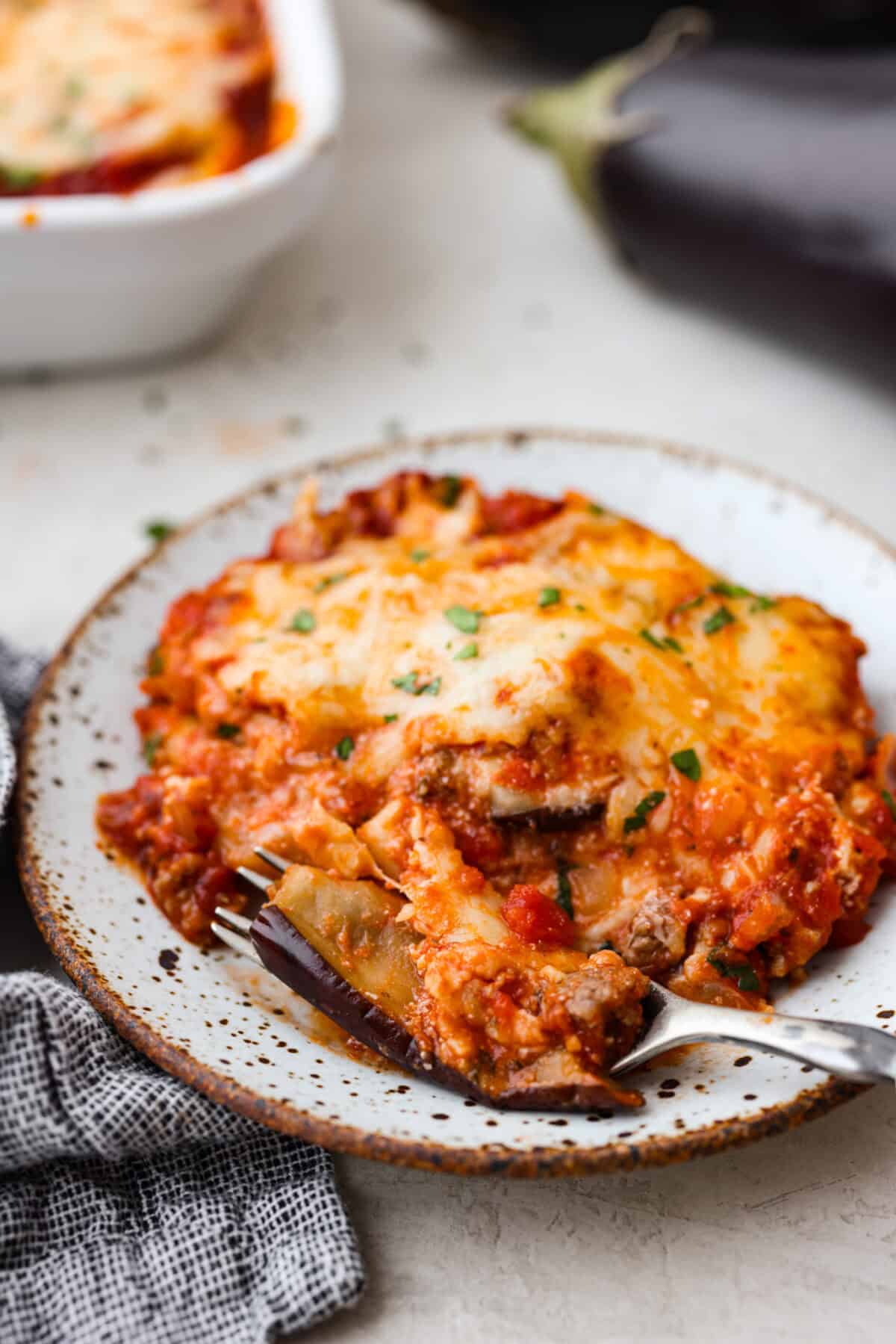 Close view of a slice of eggplant lasagna on a plate with a fork.