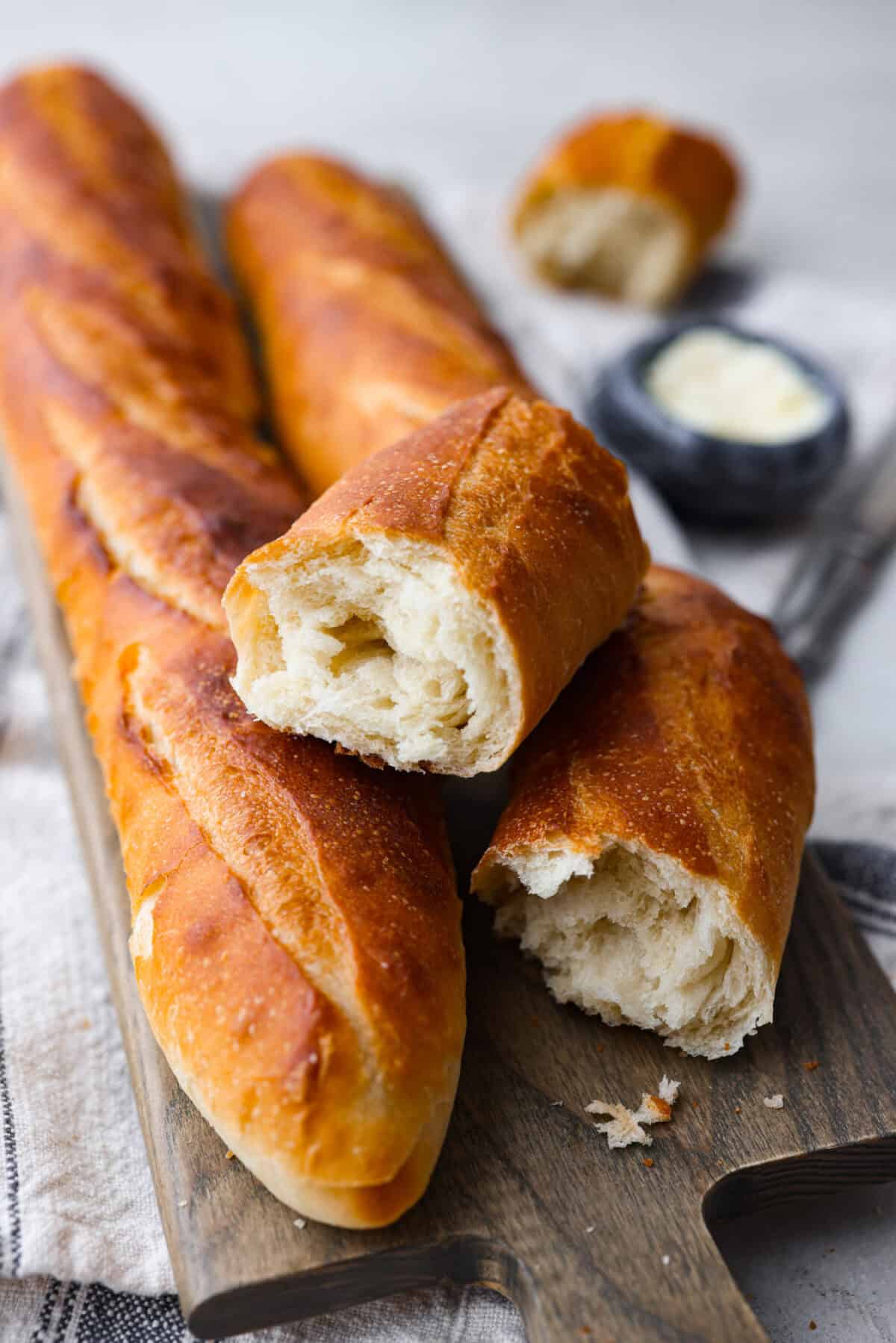 Angle shot of baguettes on a cutting board, one is pulled apart. 