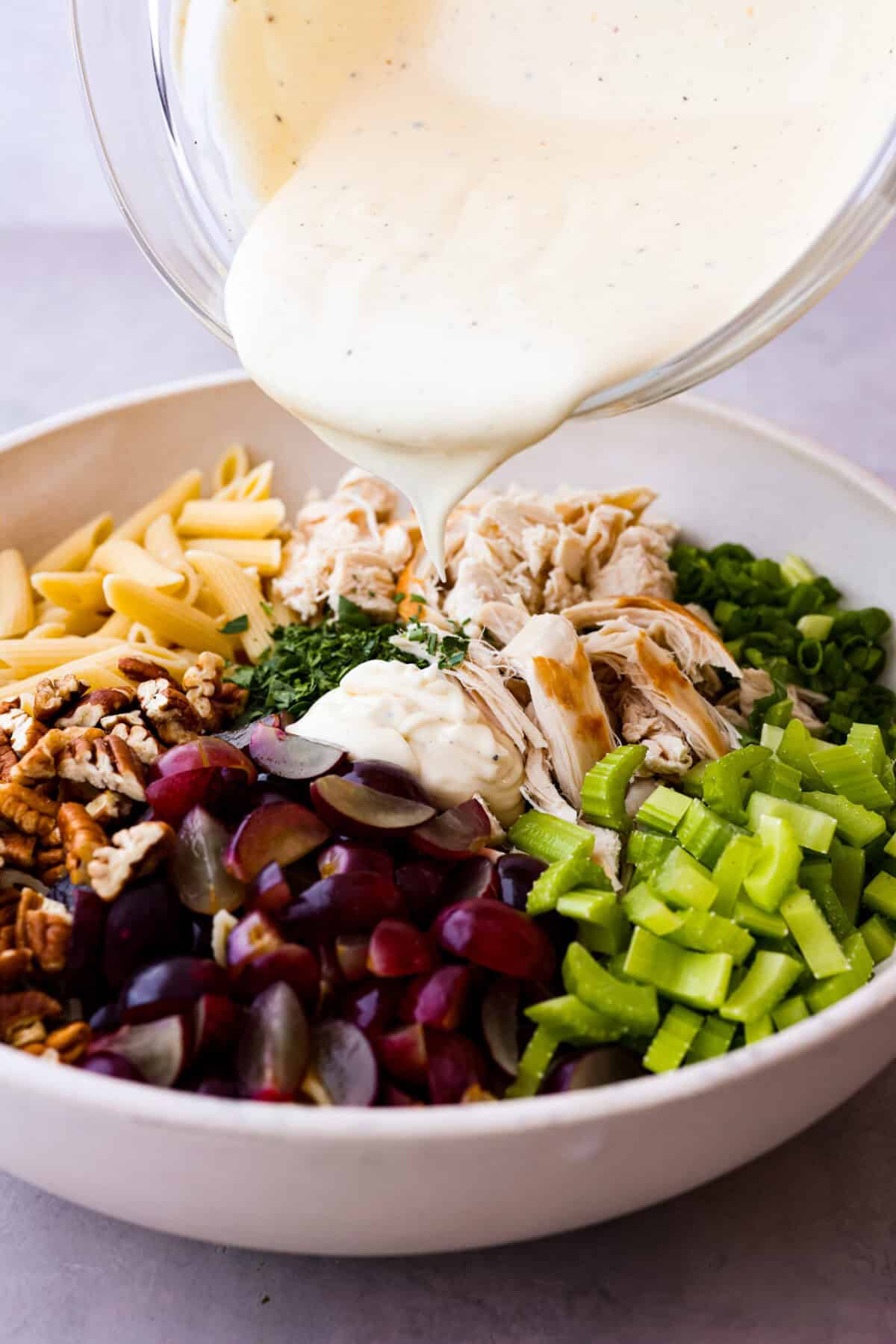 Side shot of dressing being poured over colorful pasta salad ingredients. 