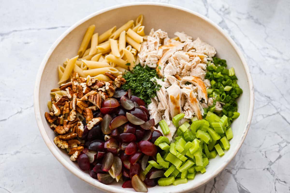 Overhead shot of bowl with pasta salad ingredients not mixed together in separate piles. 