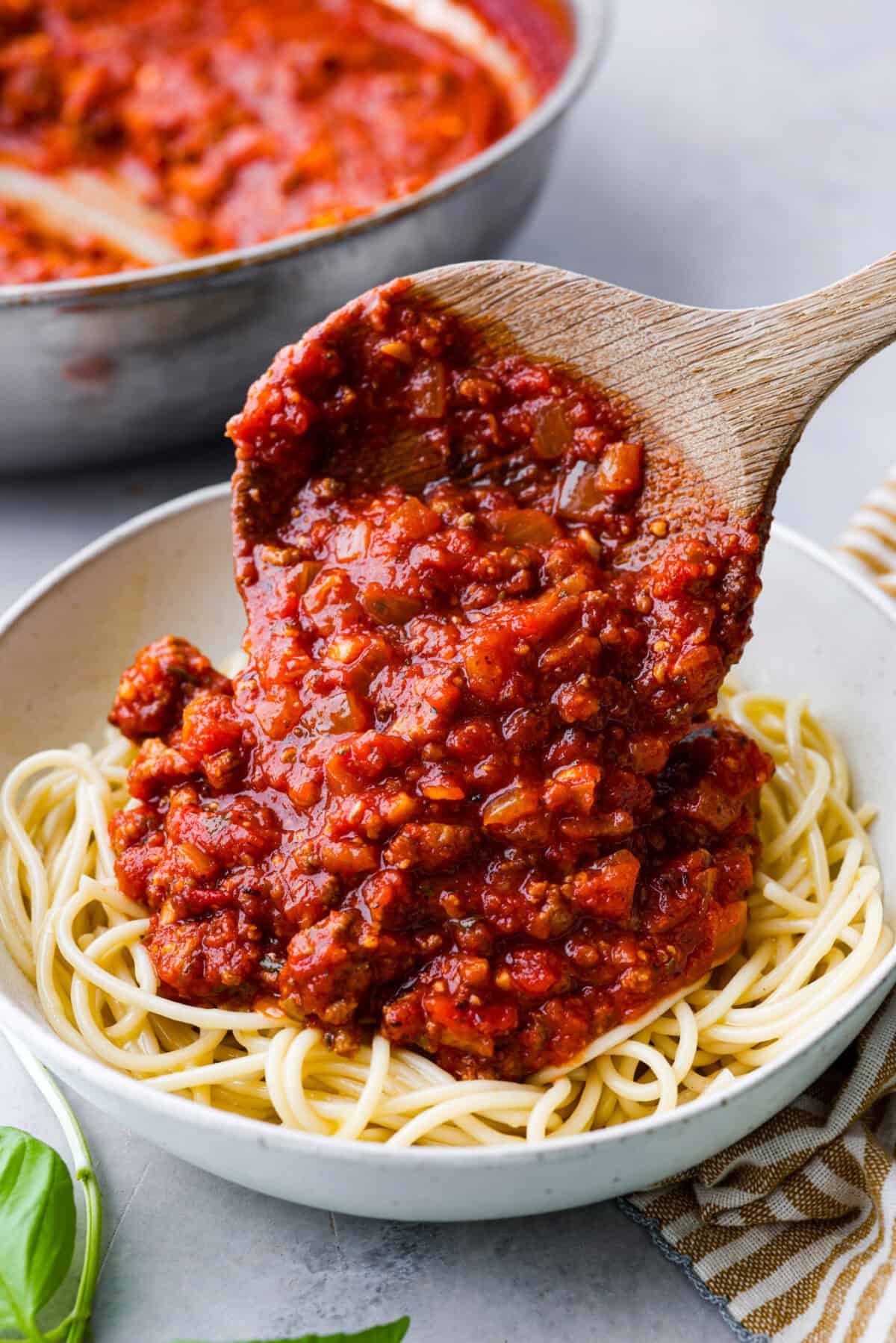 Close view of homemade spaghetti sauce spooning on top of a bowl of noodles. 