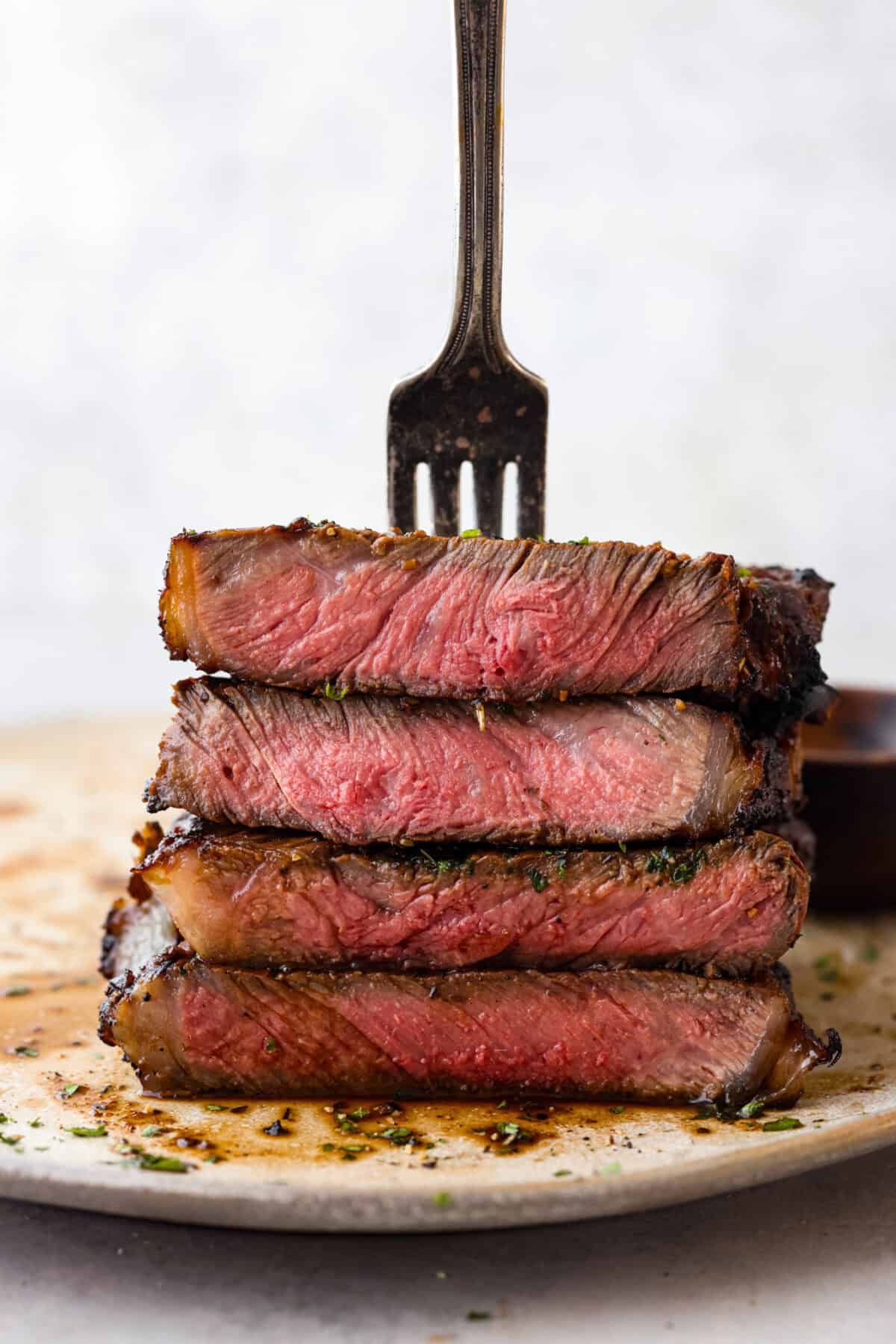 Close view of grilled stacked pieces of steak with a fork stabbing in the meat on top.