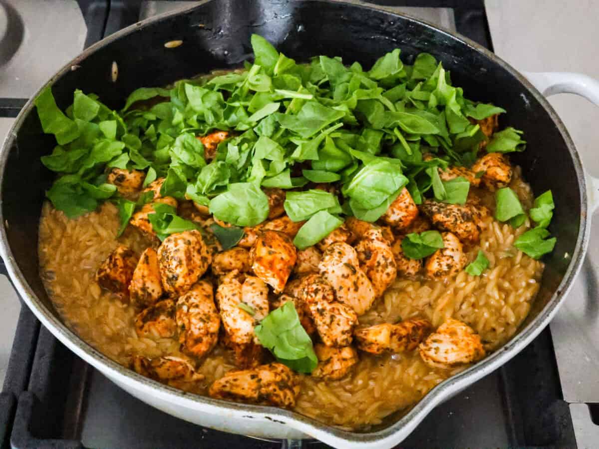 Angle shot of cooked chicken and baby spinach added to pan.