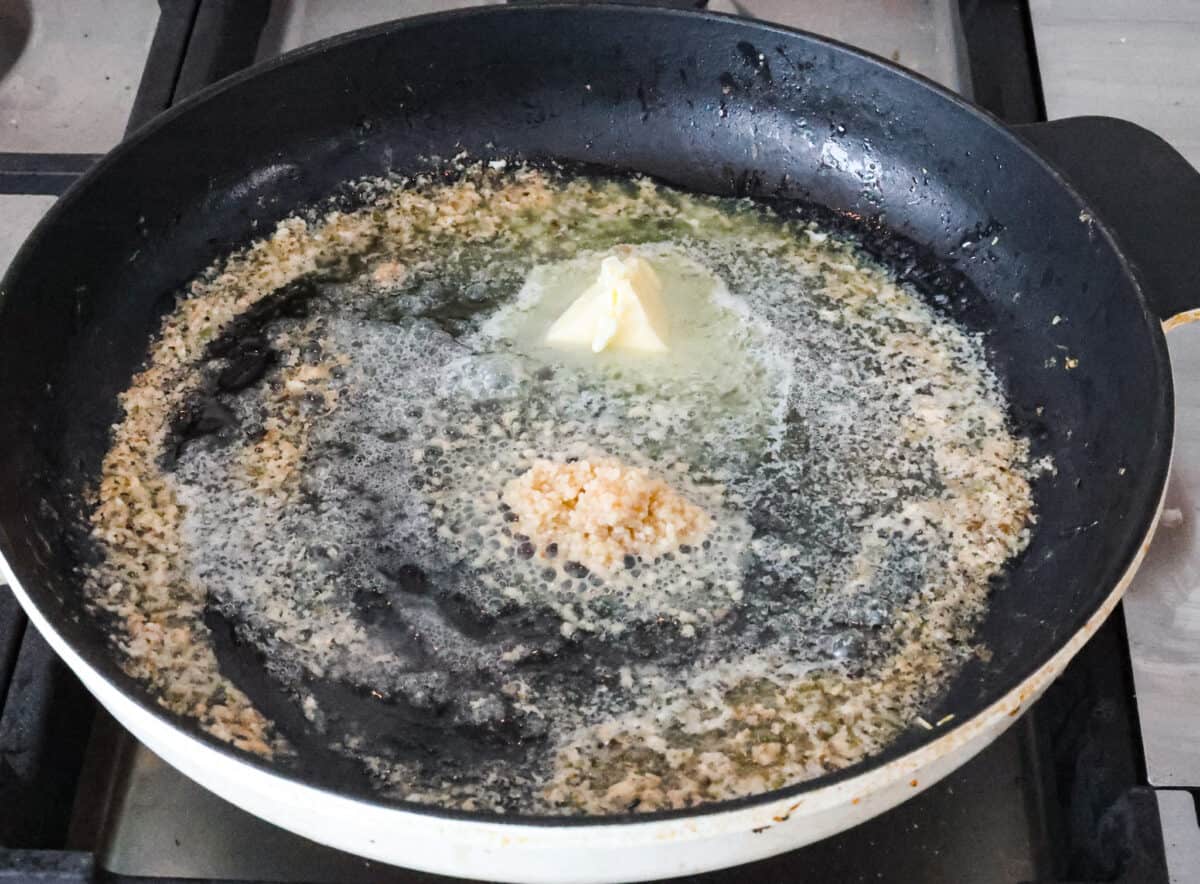 Angle shot of but and garlic sautéing in a skillet. 