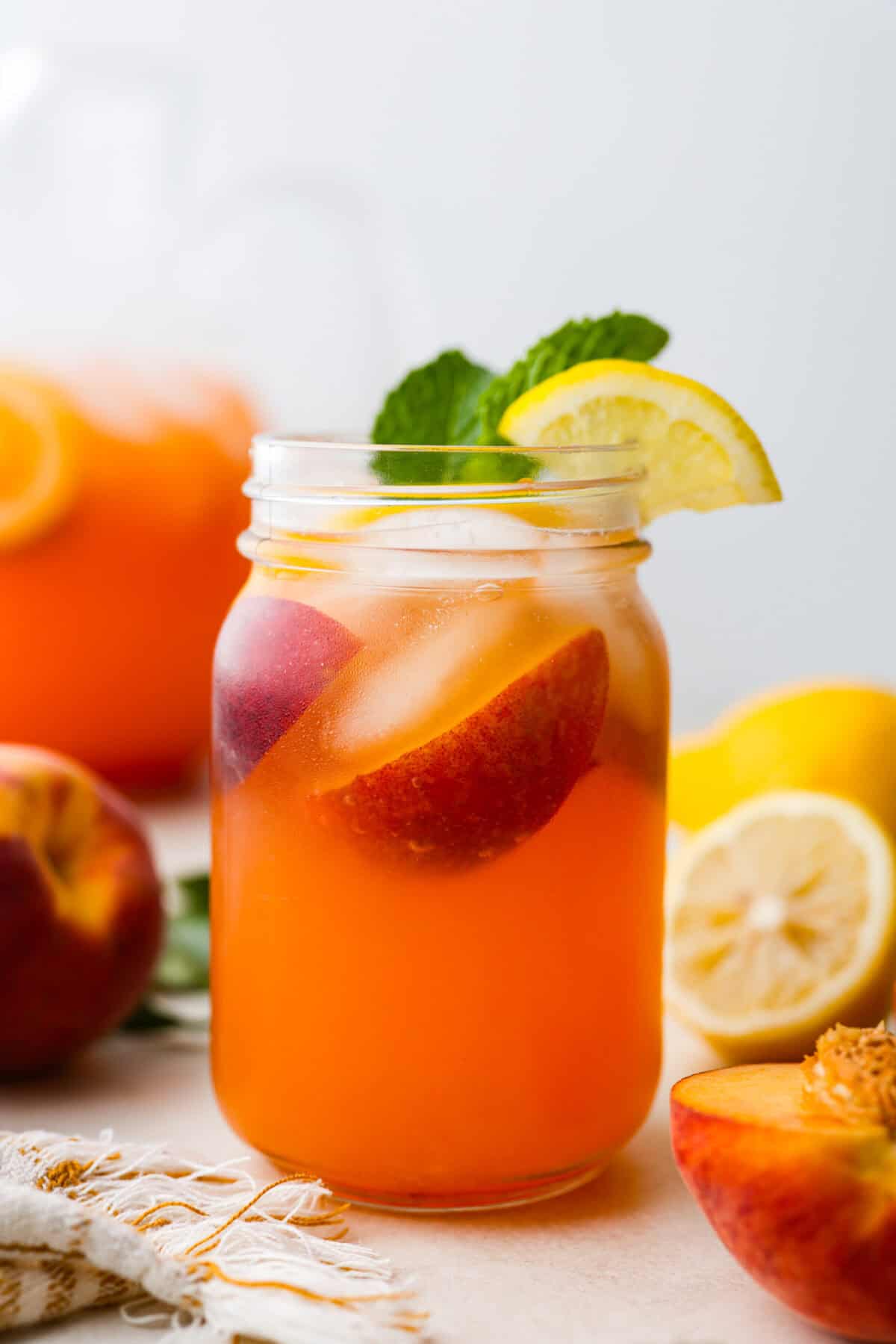 Side shot of mason jar with fresh peach lemonade with sprig of mint and garnished with a wedge of lemon. 