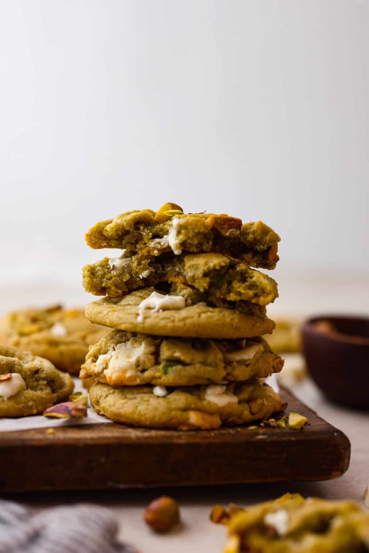 Side shot of stacked pistachio pudding cookies on a wood cutting board. 