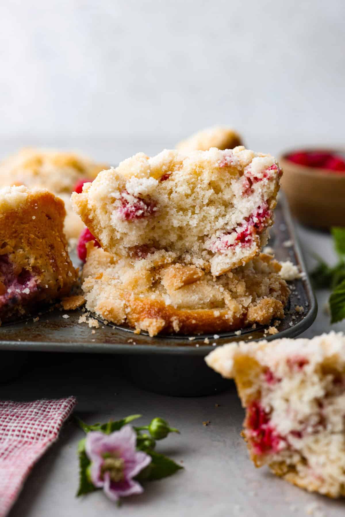 Side shot of raspberry muffin cut in half sitting on top of a pan of raspberry muffins. 