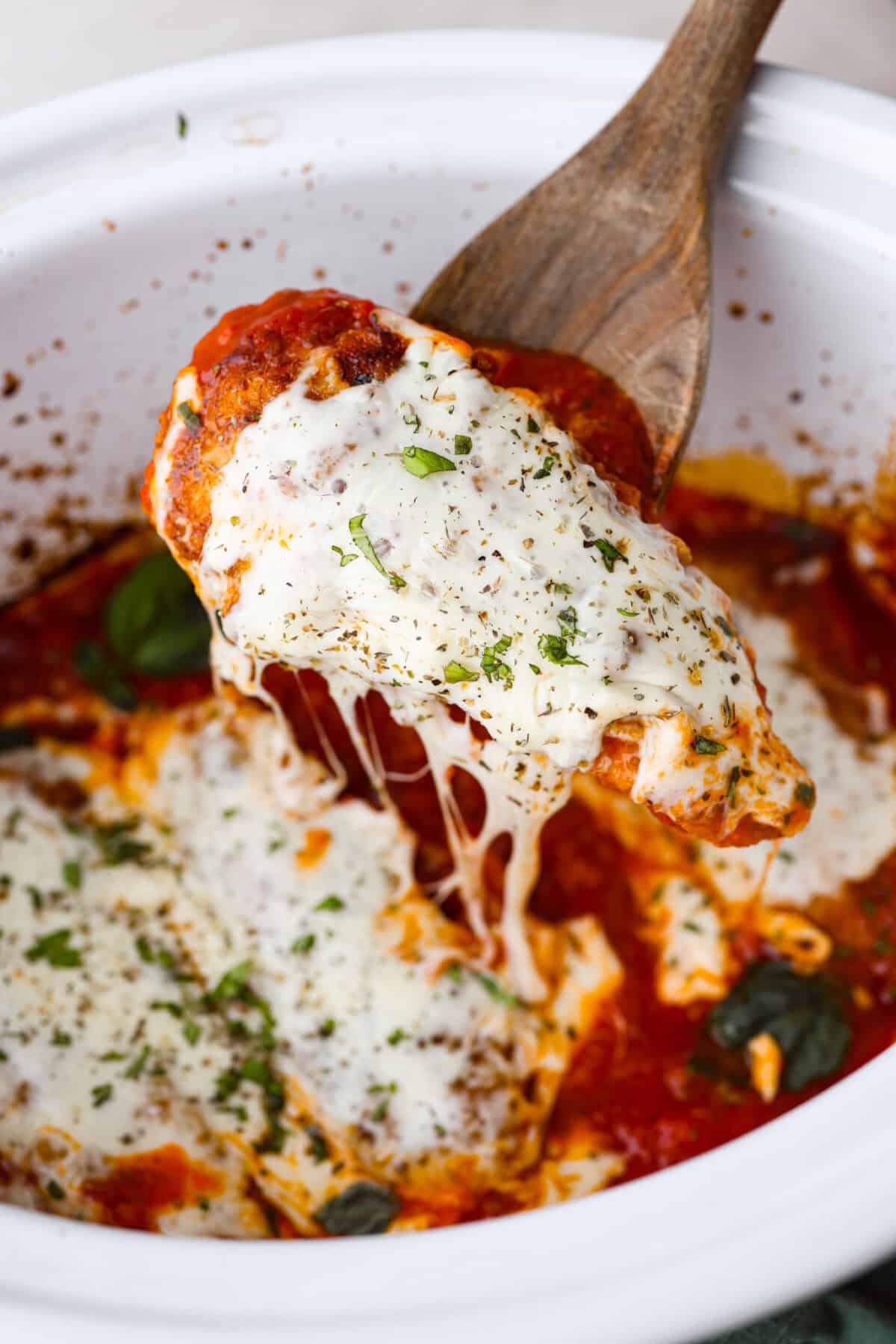 Angle shot of someone lifting a slow cooker chicken parmesan chicken tender out of the crock pot. 