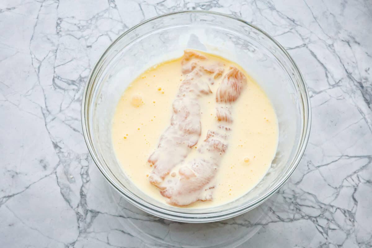 Overhead shot of bowl of egg mixture with chicken cutlets in it. 