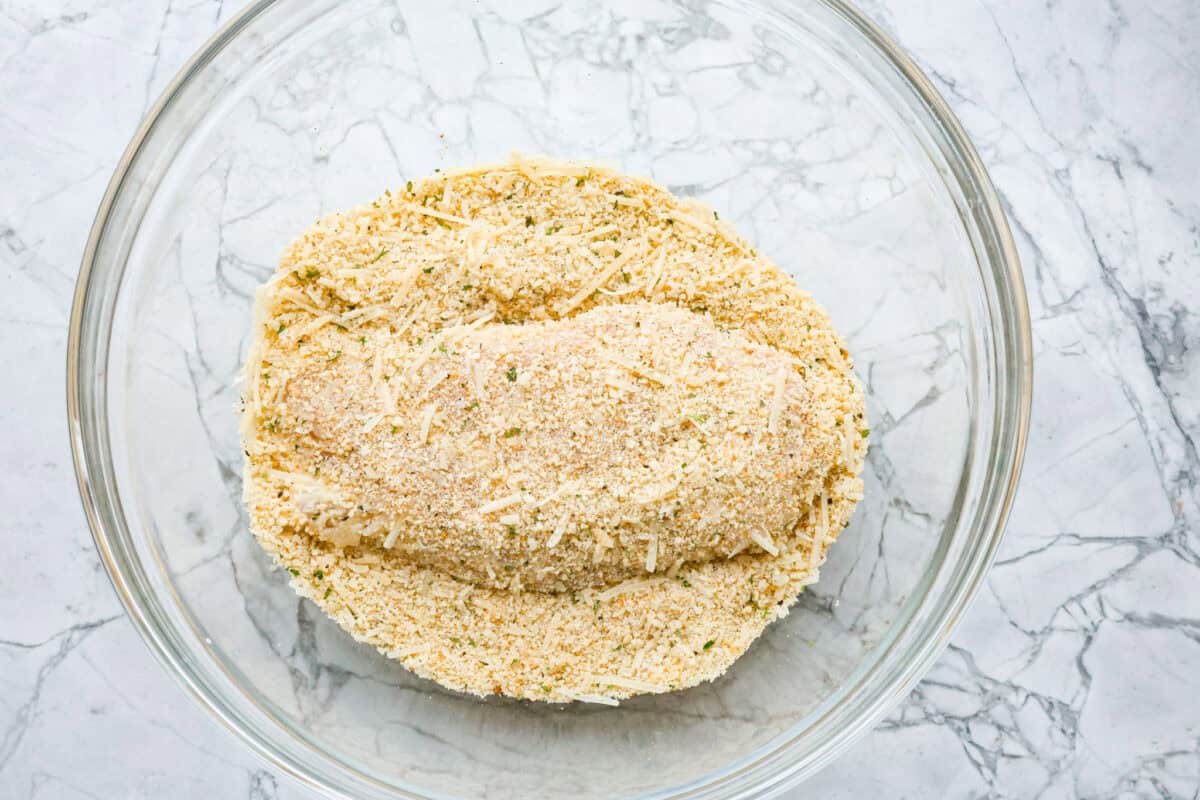 Overhead shot of chicken in breading mixture in glass bowl. 