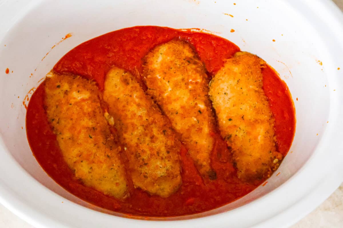 Overhead shot of crockpot filled with marinara sauce and fried chicken cutlets on top of sauce. 