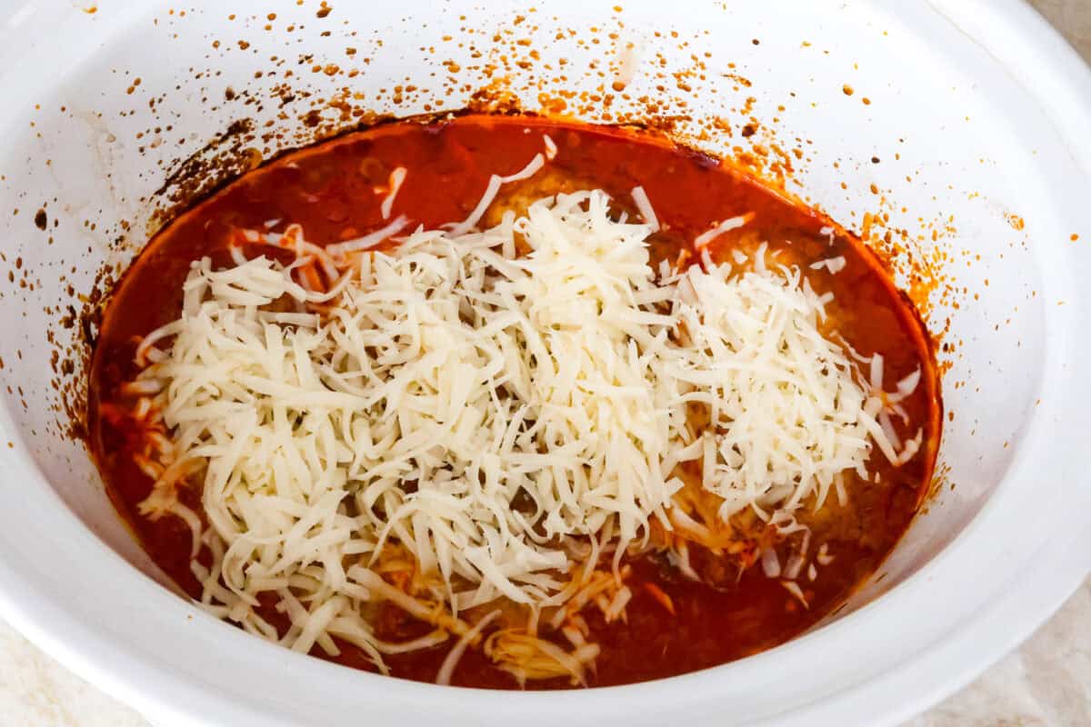 Overhead shot of cooked chicken in bottom of marinara sauce with cheese sprinkled on top. 