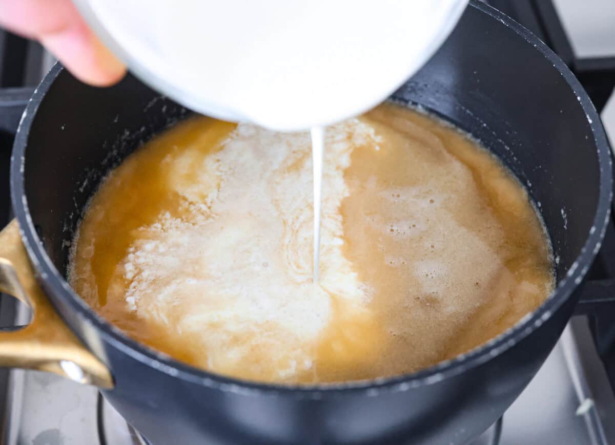 Overhead shot of someone pouring cream into the gravy mixture. 