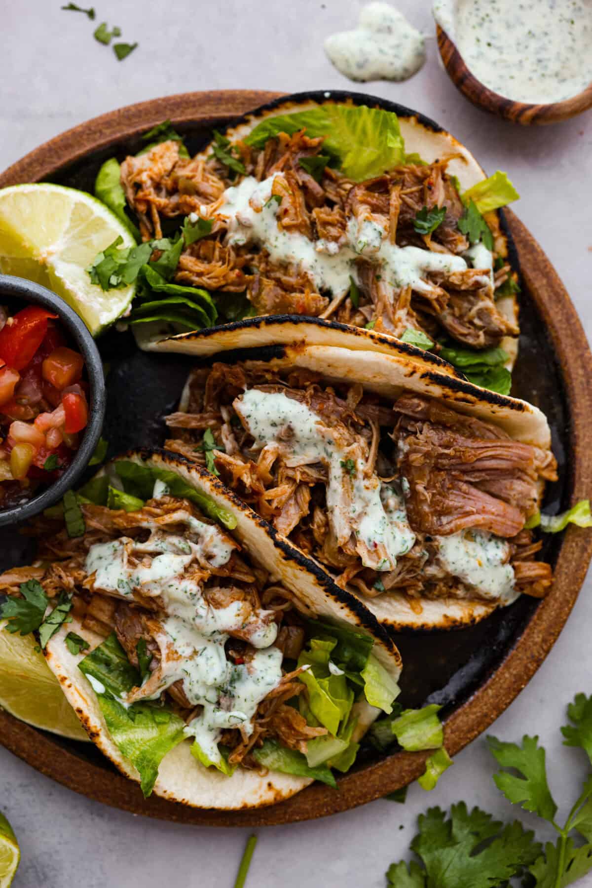 Overhead shot of sweet pork tacos on plate with lime wedges and pico de gallo. 