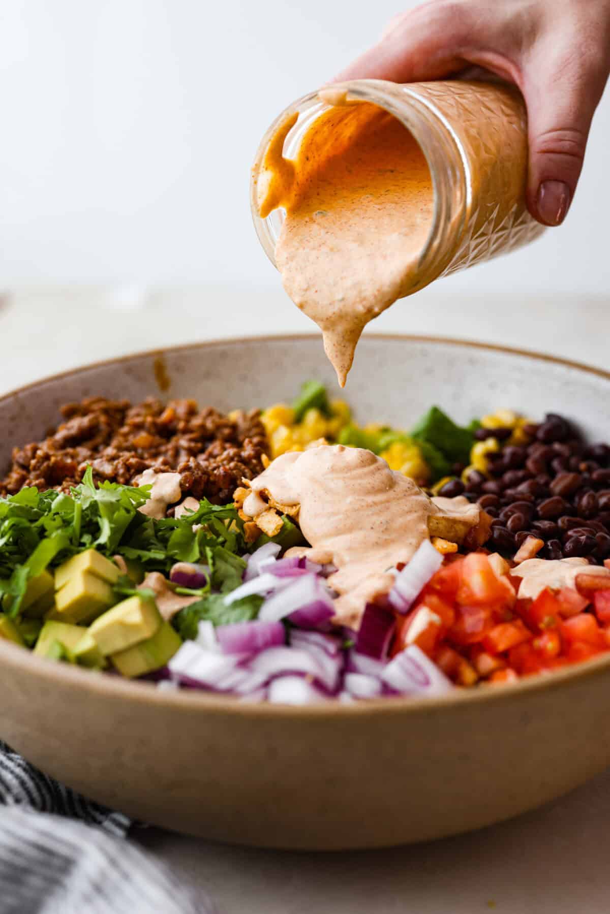 Side shot of someone pouring salad dressing of the taco salad. 