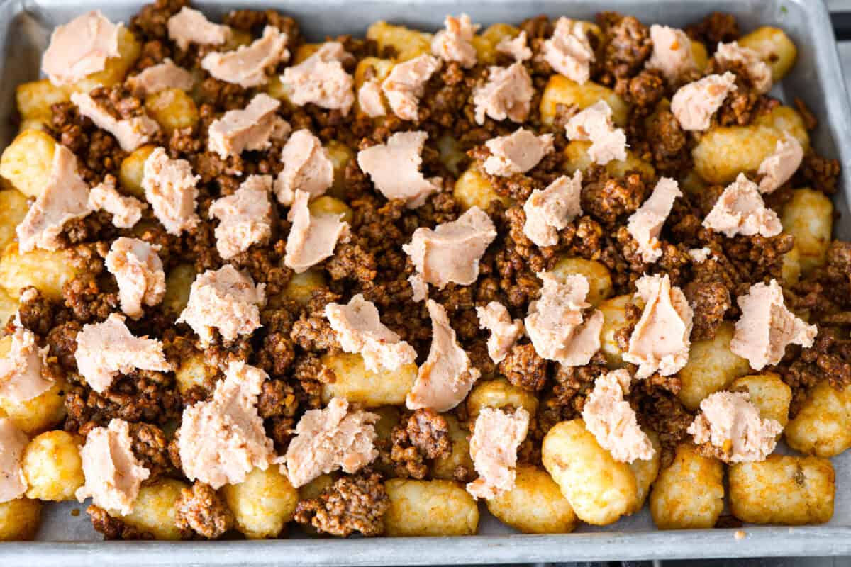 overhead shot of prepped pan full of tater tots, seasoned ground beef, and dollops of refried beans.