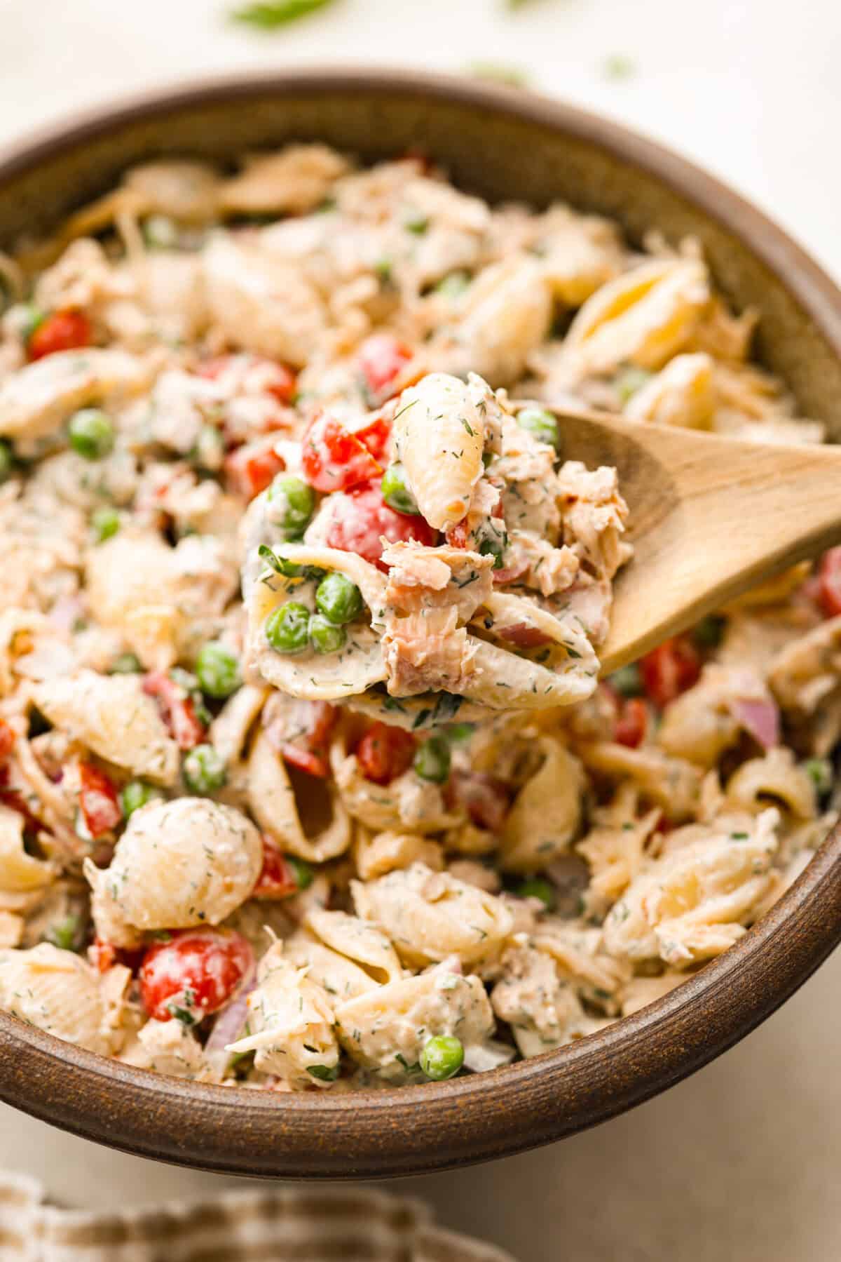 Close side view of a wood spoon lifted a scoop of tuna pasta salad.