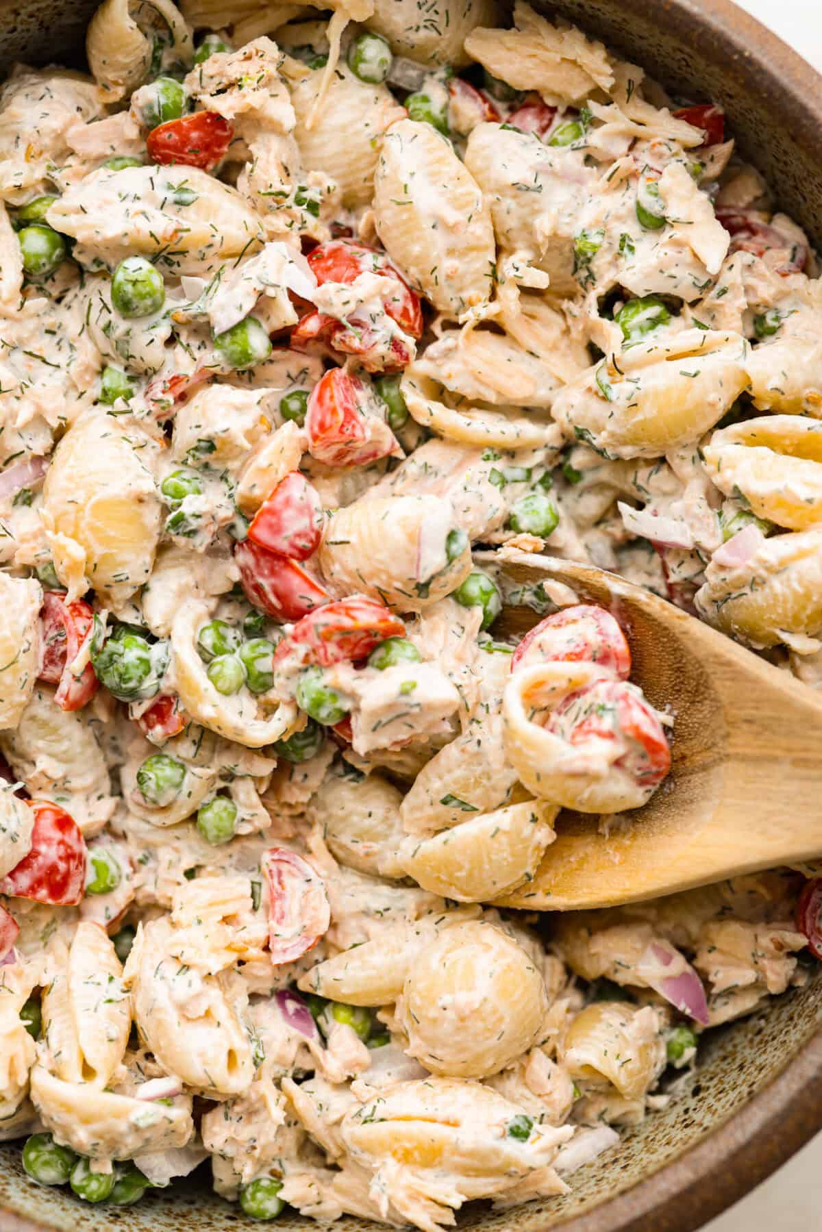 Top close view of a wood spoon in the pasta salad.