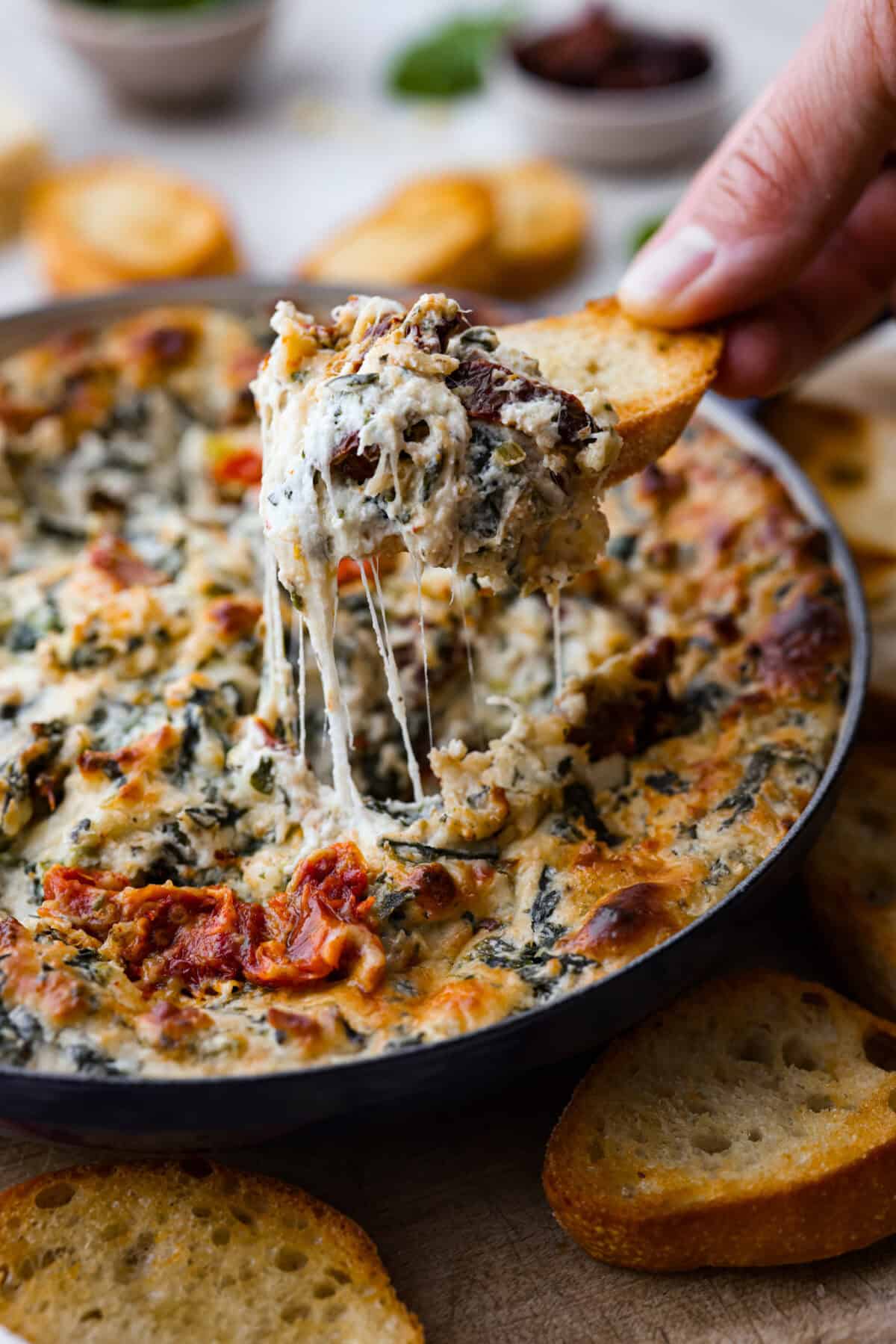 Close view of crostini dipping into a the dip with a cheese pull.