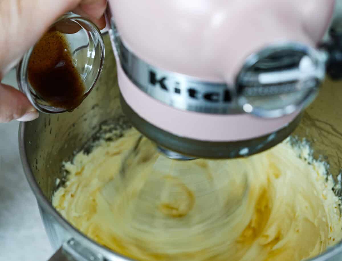 Vanilla being poured into stand mixer bowl whipping frosting. 