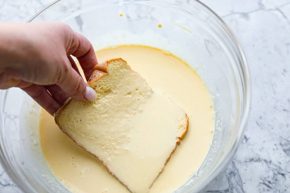 Fourth photo of the bread being dipped into the egg mixture.