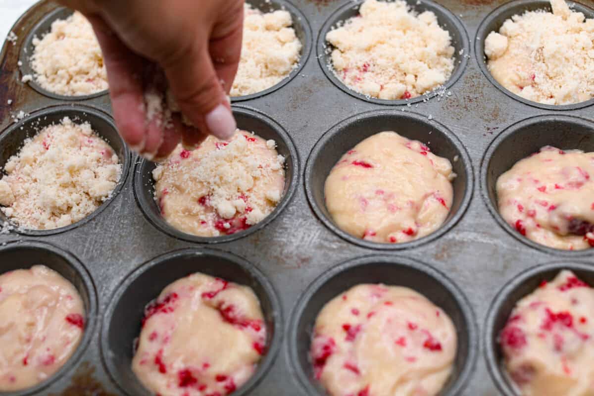 Angle shot of someone sprinkling streusel  over muffin batter in muffin tin. 