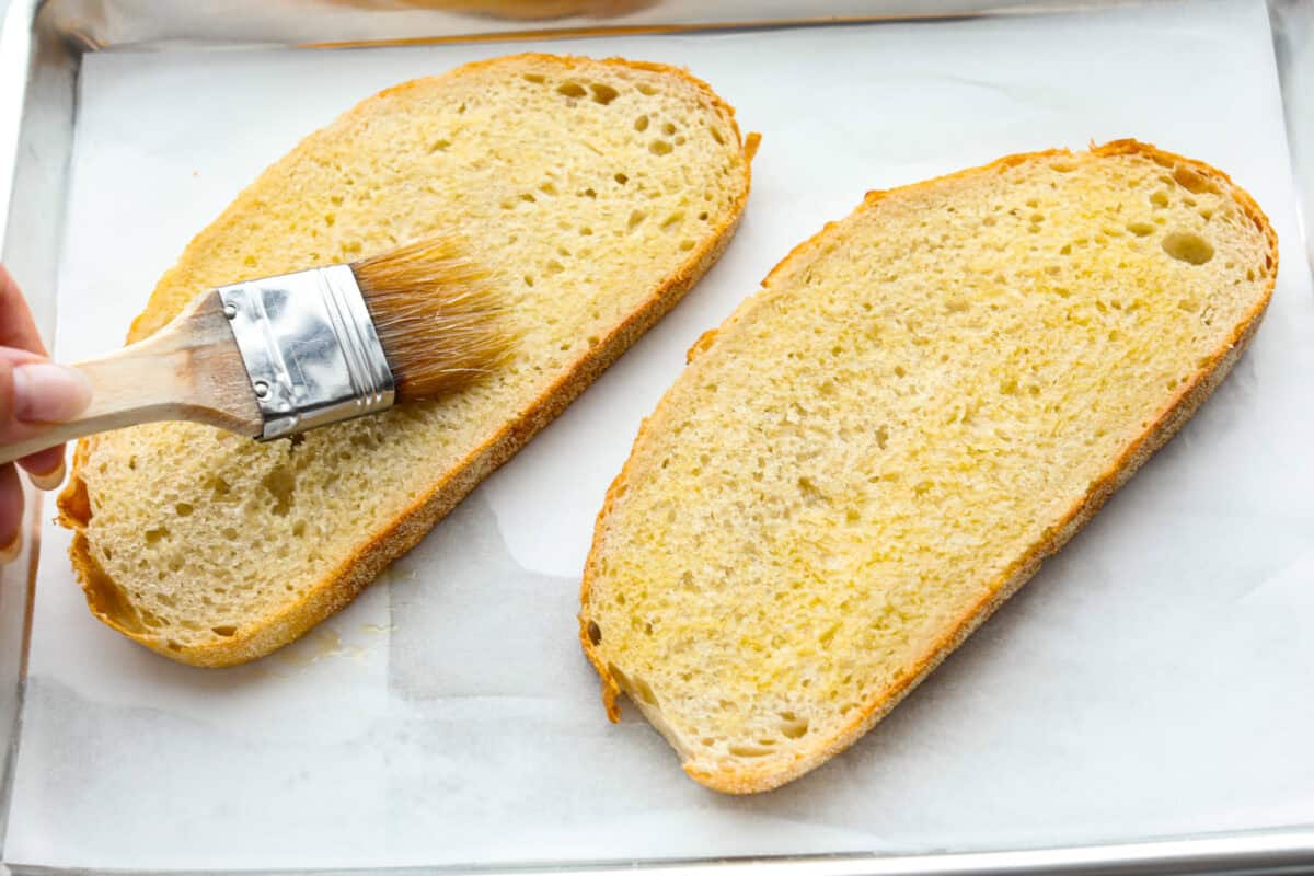 Overhead shot of someone brushing olive oil on slices of bread. 