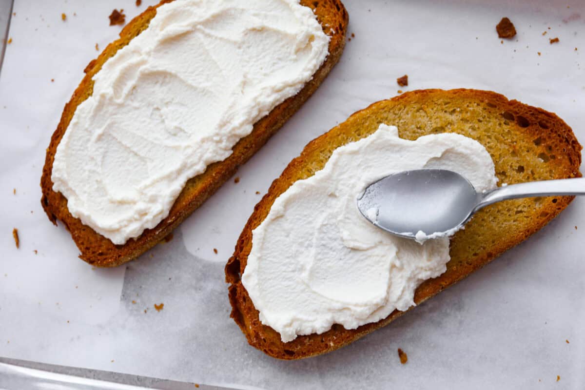 Overhead shot of someone spreading ricotta over toasted bread. 