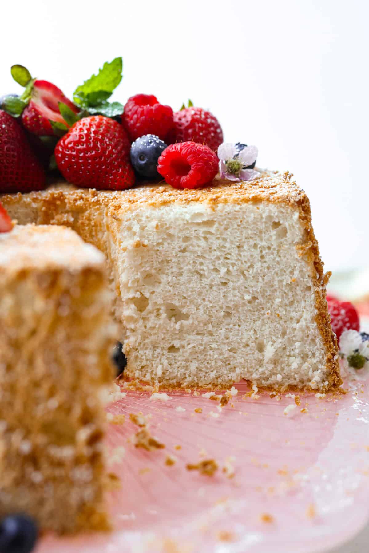 Side shot of angel food cake covered in berries with a slice taken out of it. 