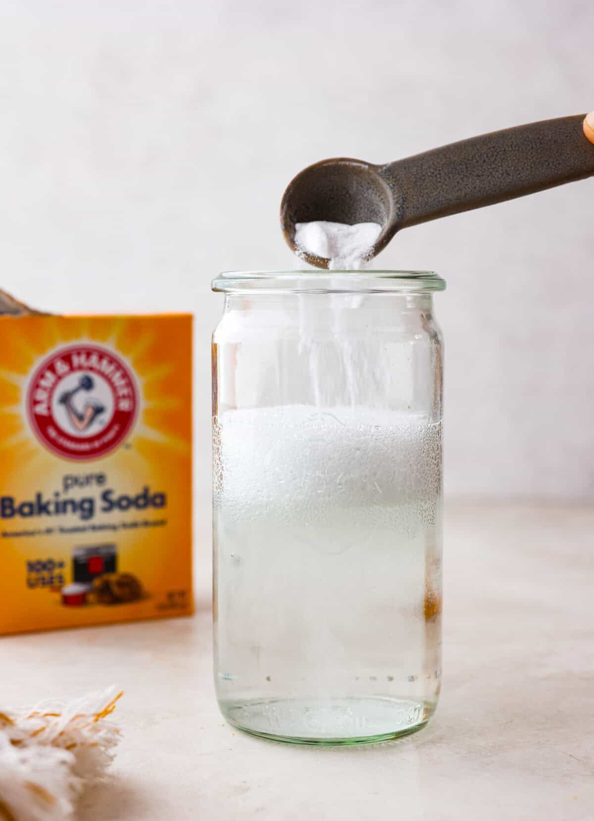 Side view of baking soda going into a glass jar of vinegar and bubbling up.