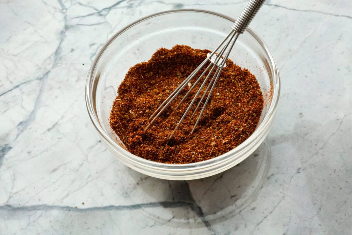 Overhead shot of chipotle seasoning ingredients in a glass bowl with a whisk sticking out of it. 