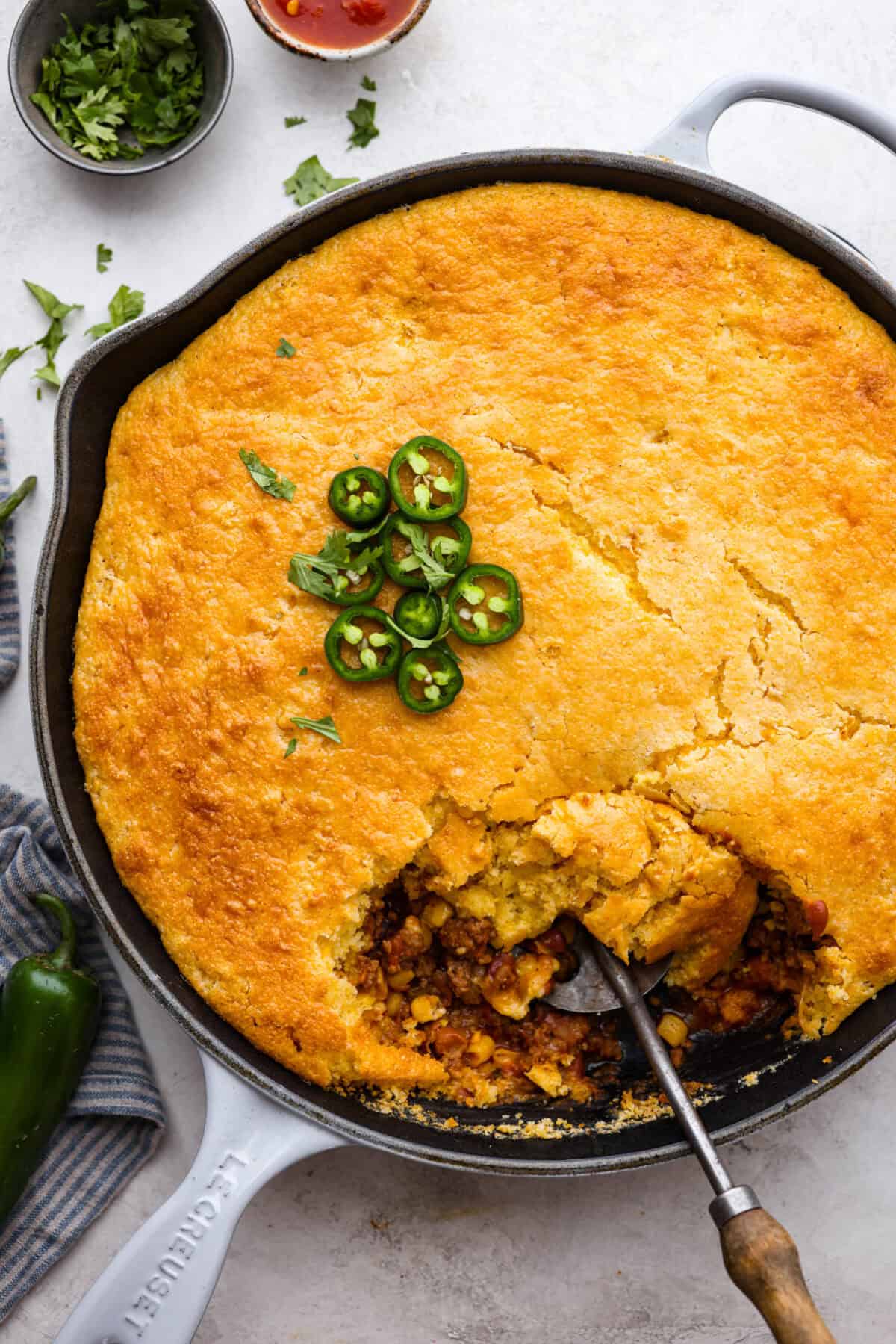 Overhead shot of cowboy cornbread casserole with a garnish jalapeños on top and a spoon scooping some out. 