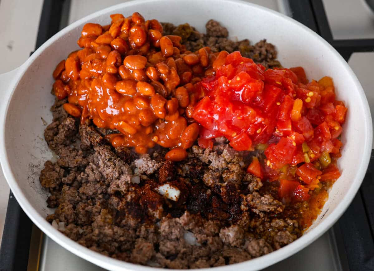 Angle shot of ground beef mixture with can of beans and Rotel dumped over the top. 