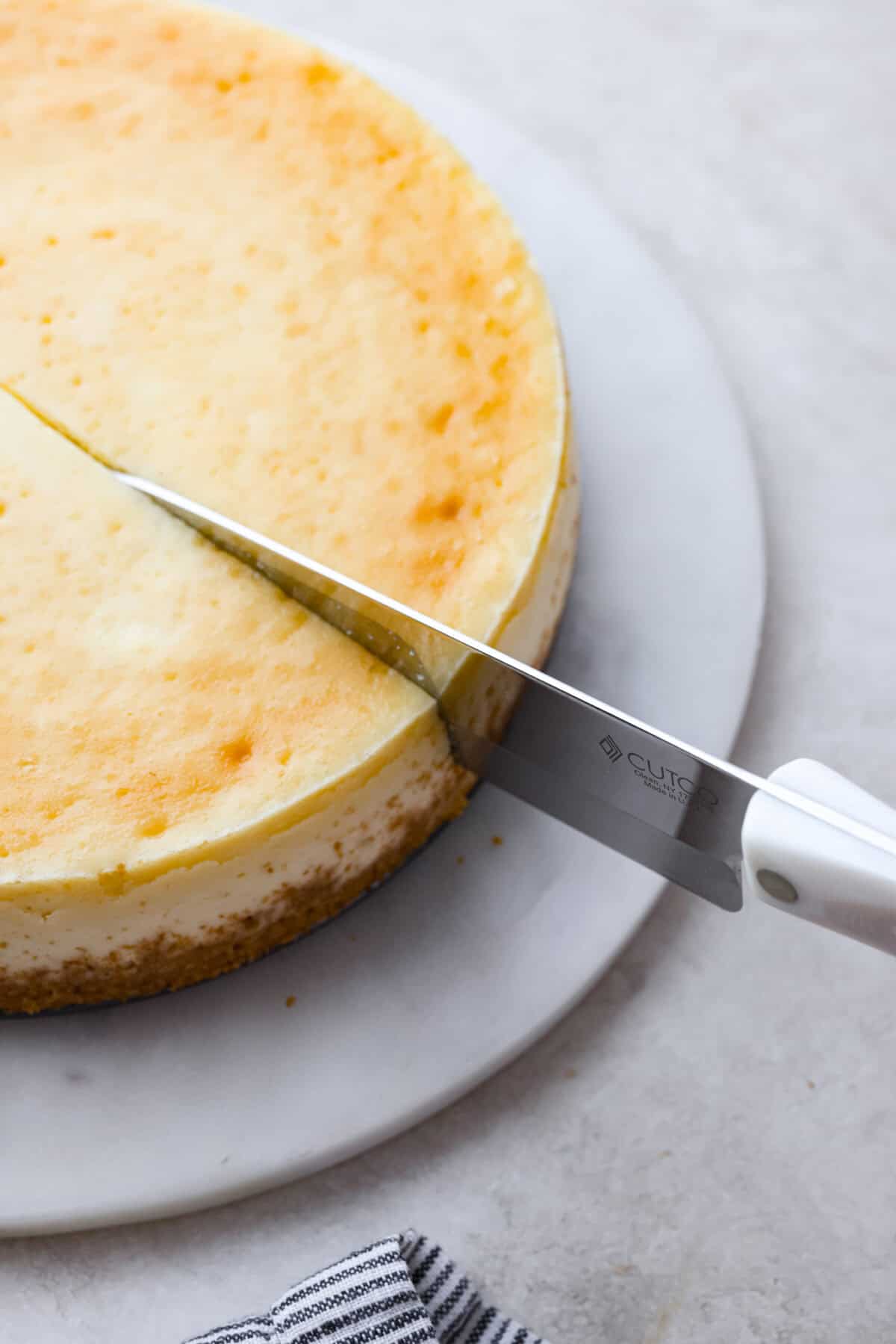 Second photo of a large knife cutting a slice of cheese.