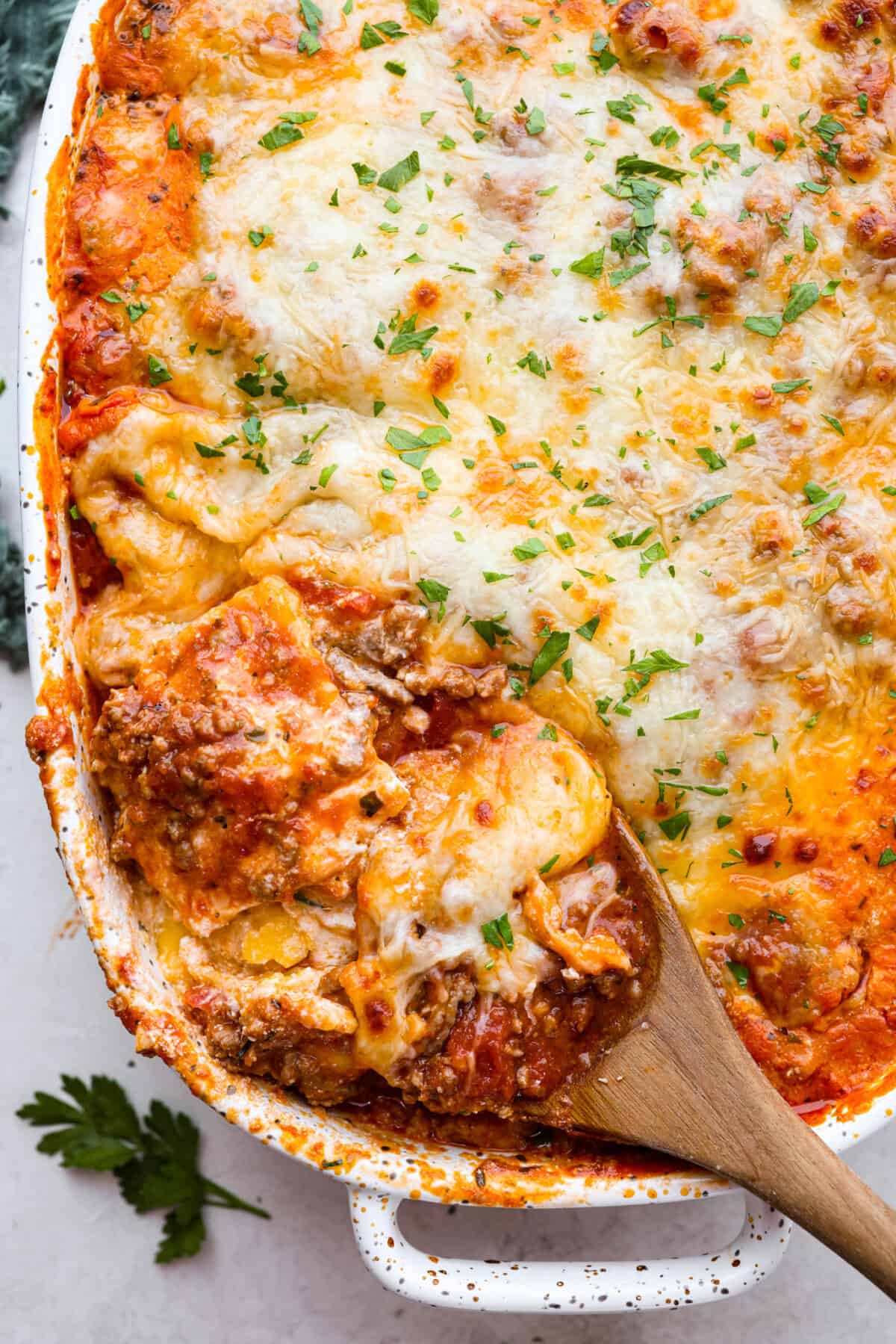 Overhead shot of million dollar ravioli casserole with wooden spoon scooping out a portion. 