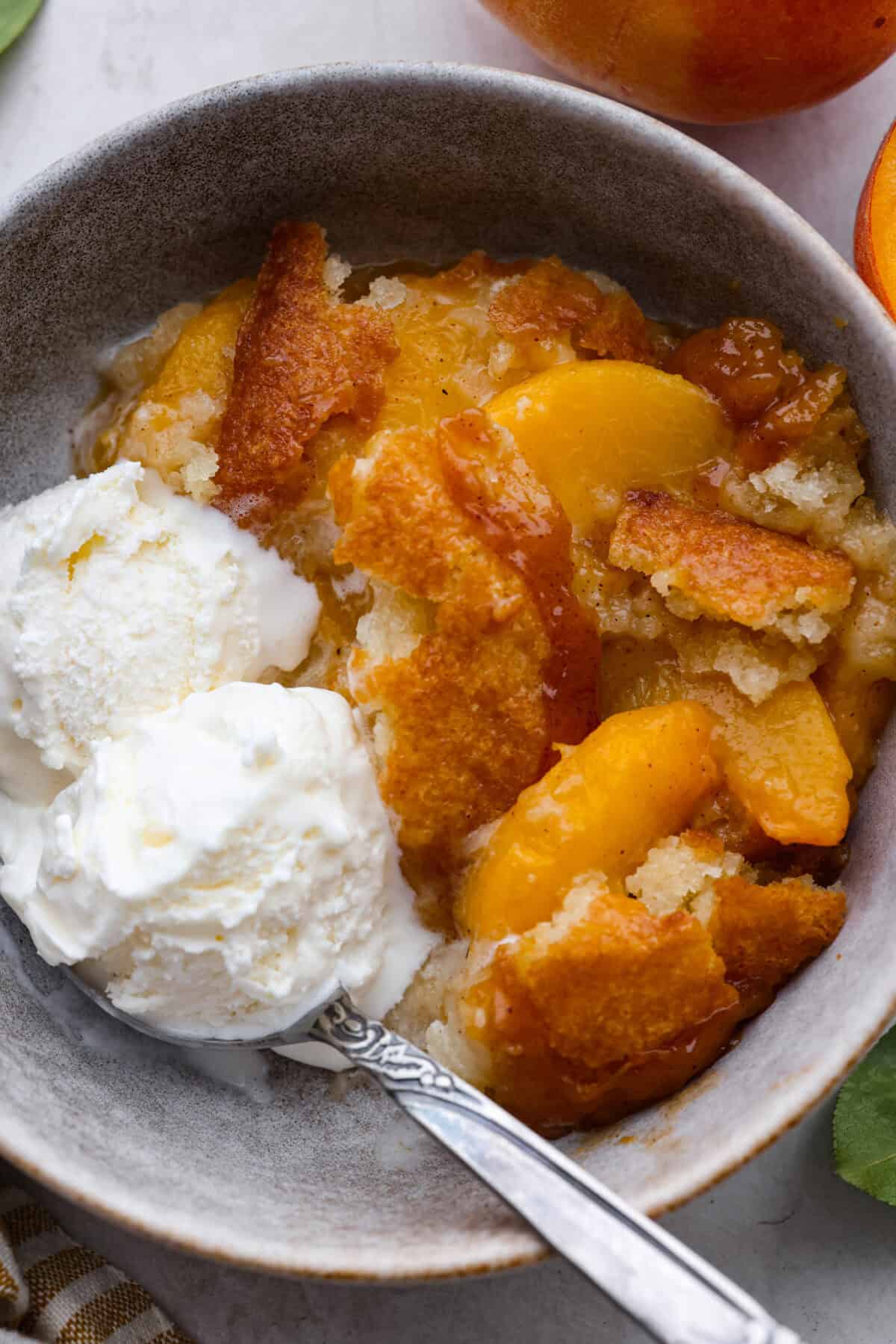 Overhead shot of a bowl of old fashioned peach cobbler with a scoop of vanilla ice cream. 