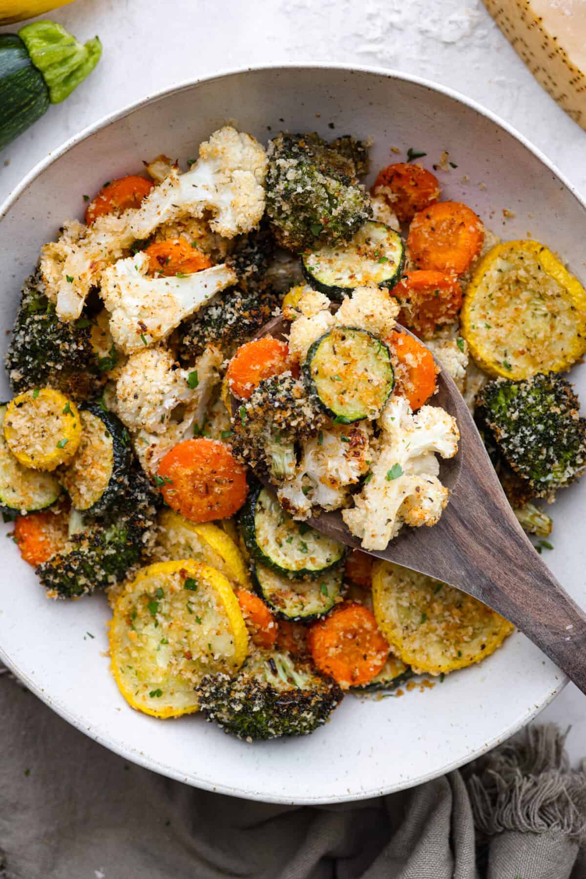 Overhead shot of parmesan roasted vegetables with wooden spoon. 