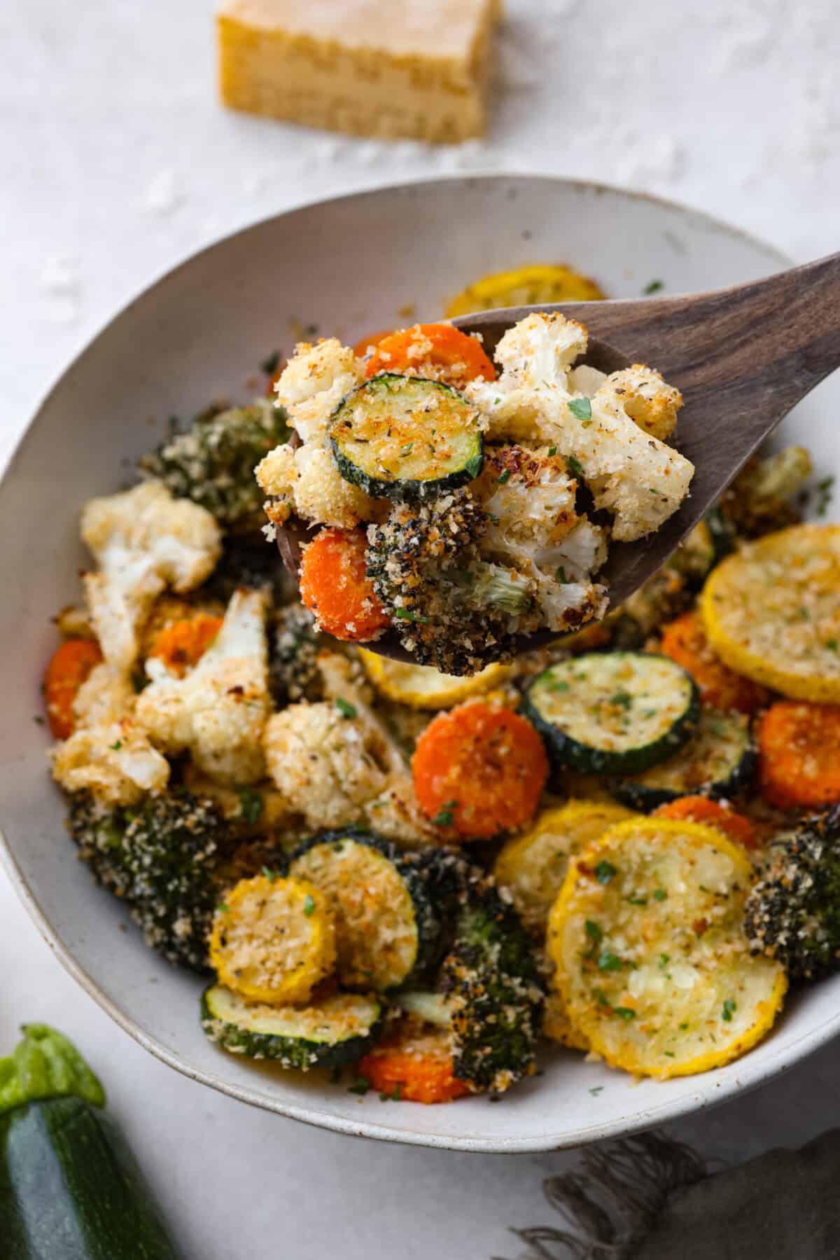 Close up shot of a wooden spoon filled with parmesan roasted vegetables. 