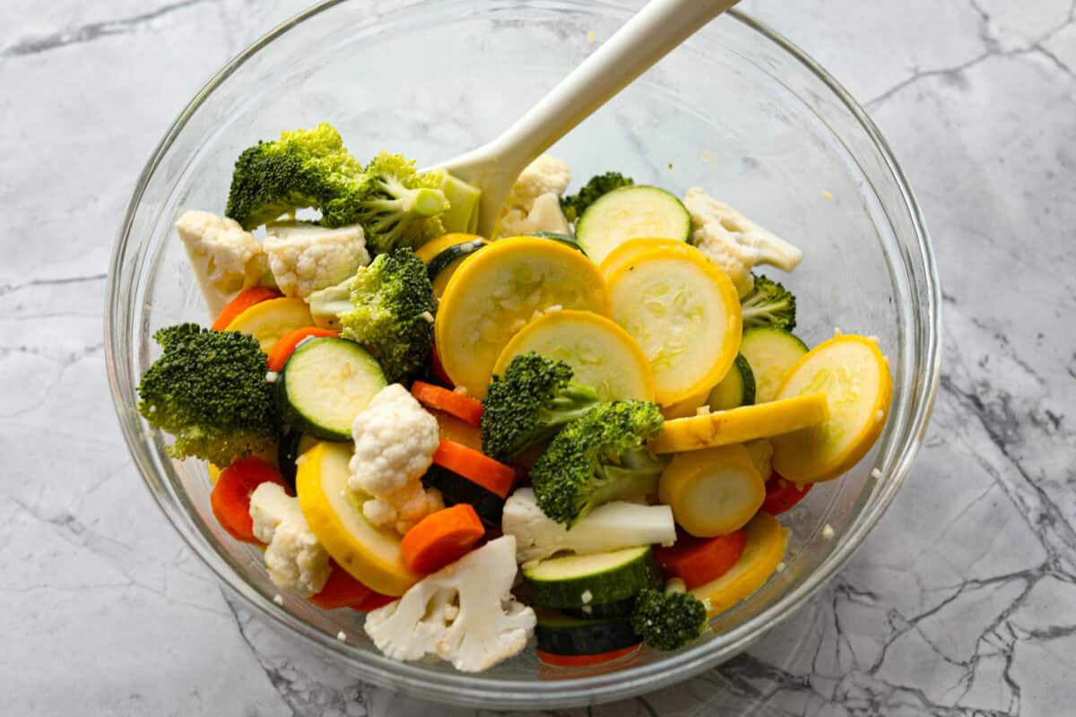 Overhead shot of vegetables in glass bowl being mixed with olive oil and butter mixture. 