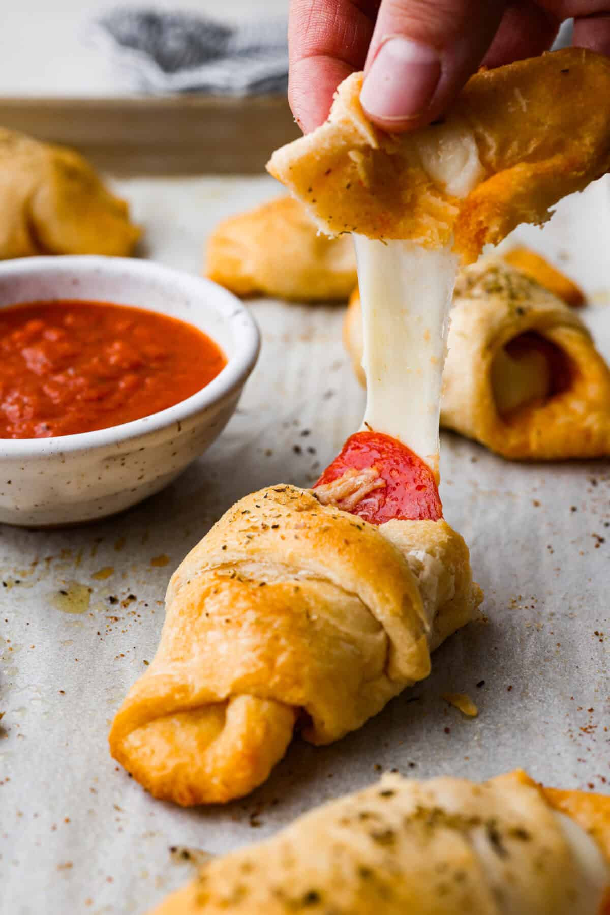 Side shot of someone pulling apart a pizza stuffed crescent roll with a cheese pull. 