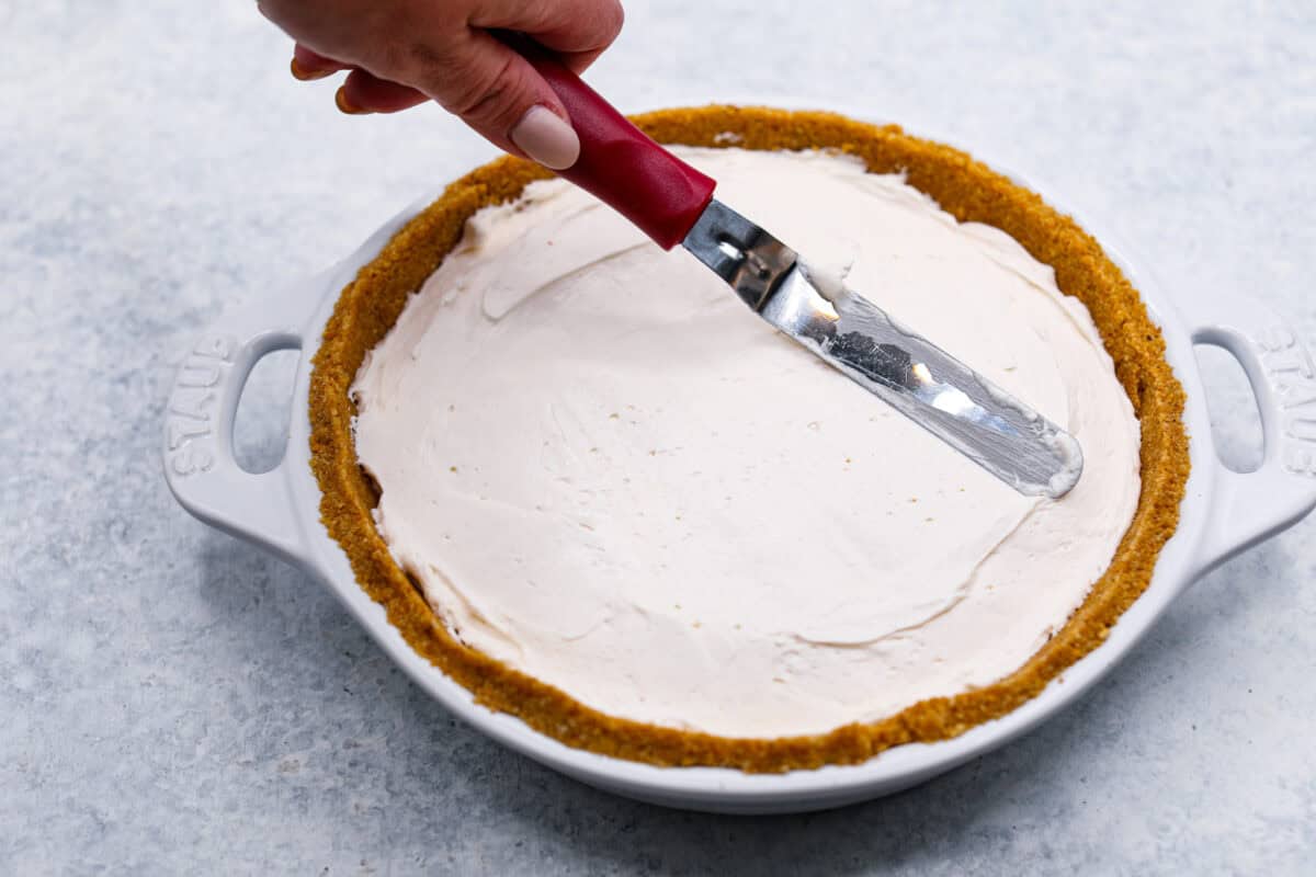 Angle shot of someone smoothing out the cream filling into the fresh peach pie crust. 