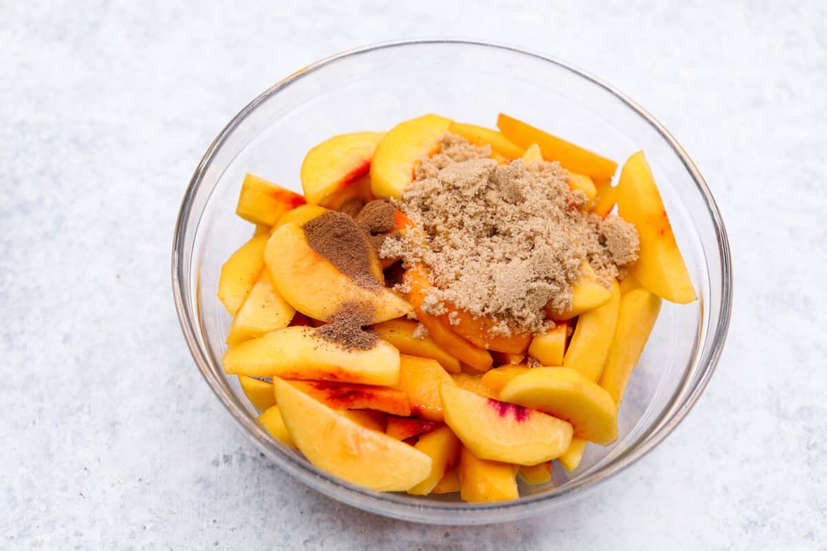 Overhead shot of a bowl of sliced peaches with brown sugar, cinnamon and nutmeg  on top. 