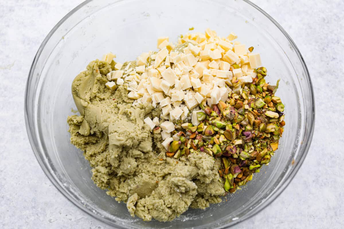 Overhead shot of the pistachio pudding cookie dough with white chocolate chunks and pistachios in a mixing bowl. 