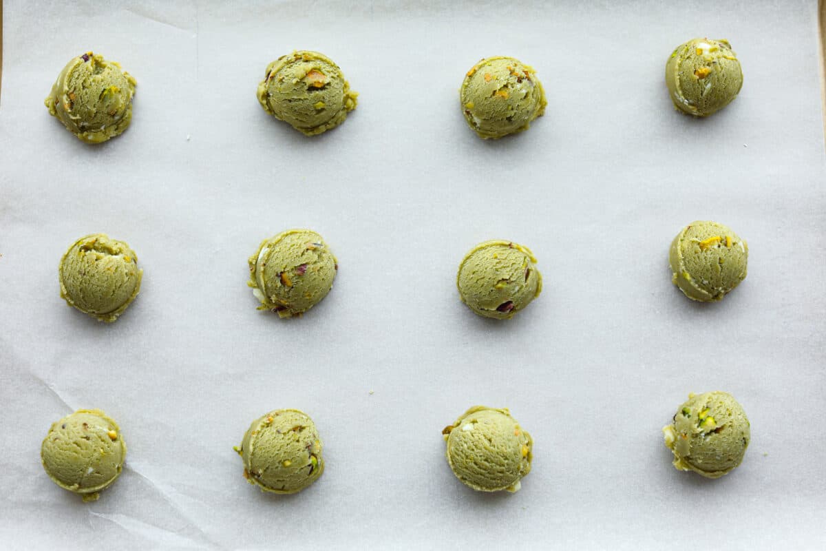 Overhead shot of cookie dough scooped into balls spread out on a cookie sheet covered in parchment paper. 