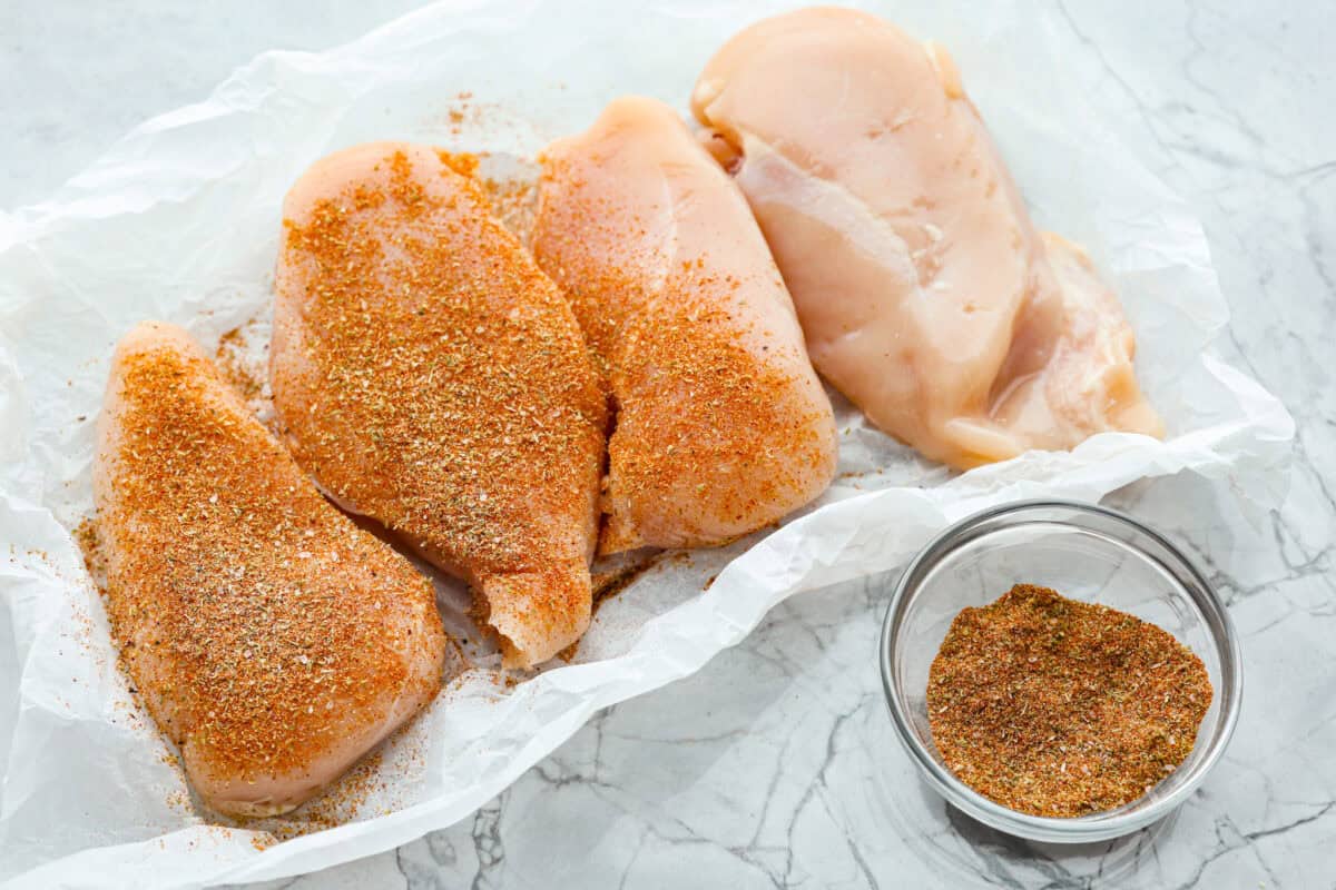 Overhead shot of chicken breasts being covered in seasonings. 